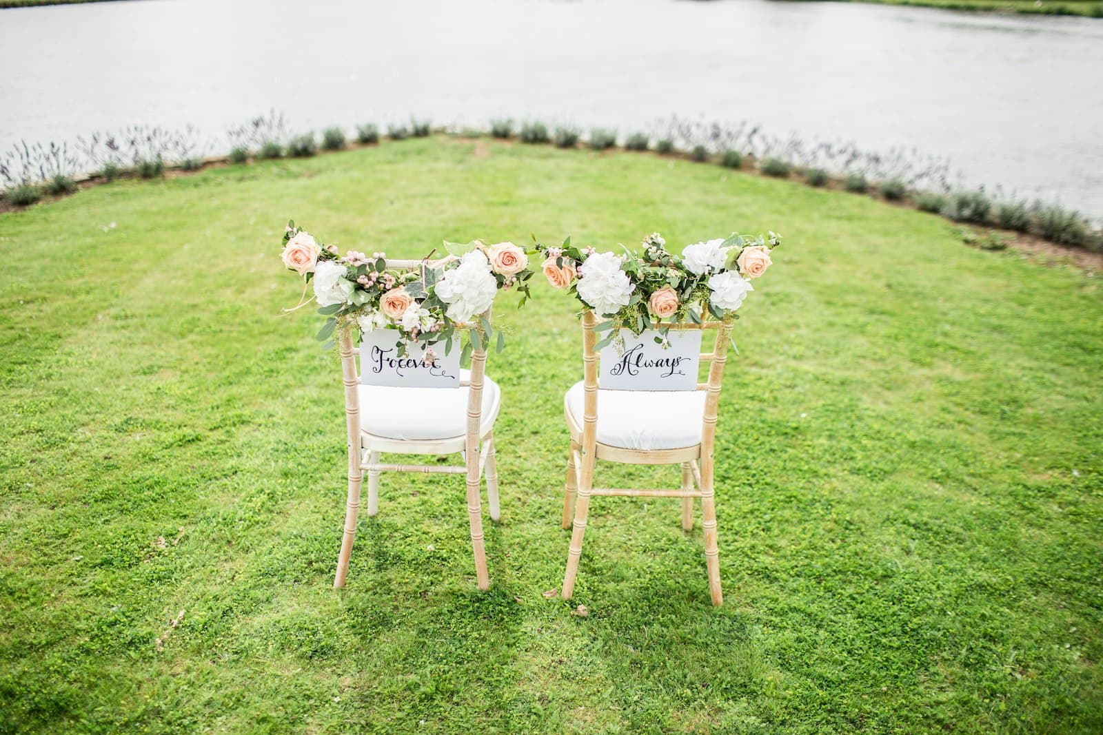 Two flower-decorated chairs on a lawn by the water