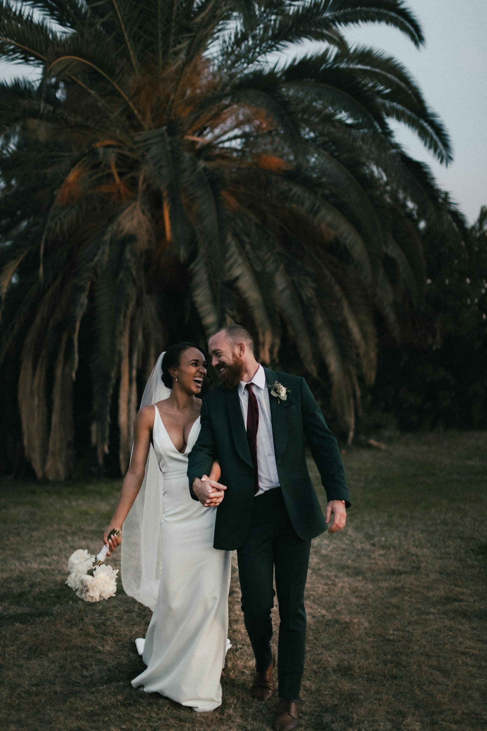 Couple walking hand in hand under a large palm tree